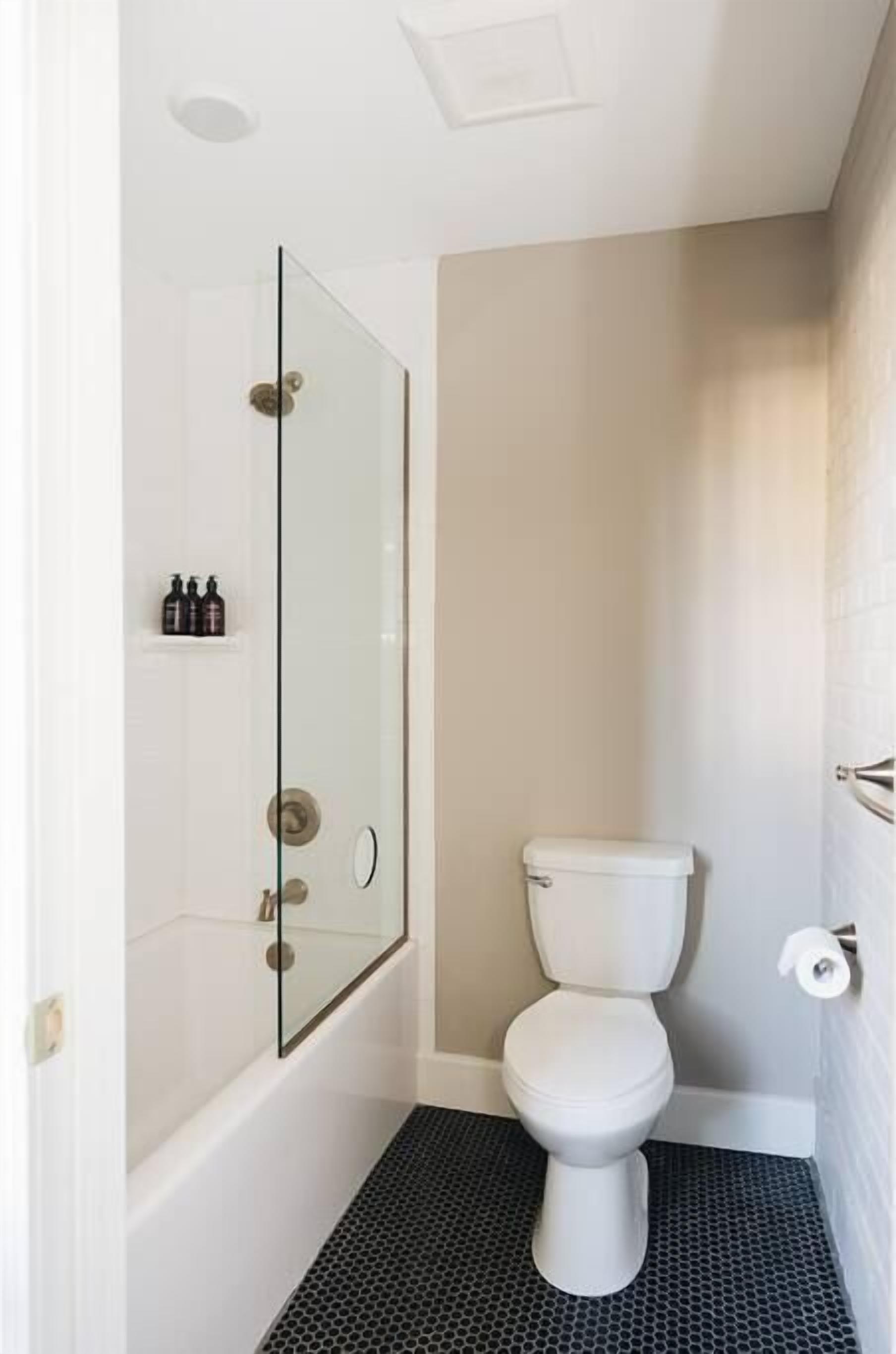 Een badkamer met een douchecabine van glas, een wit toilet en een vloer betegeld met zwart.