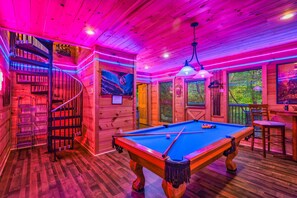 A pool table in a room with wooden walls and a spiral staircase.