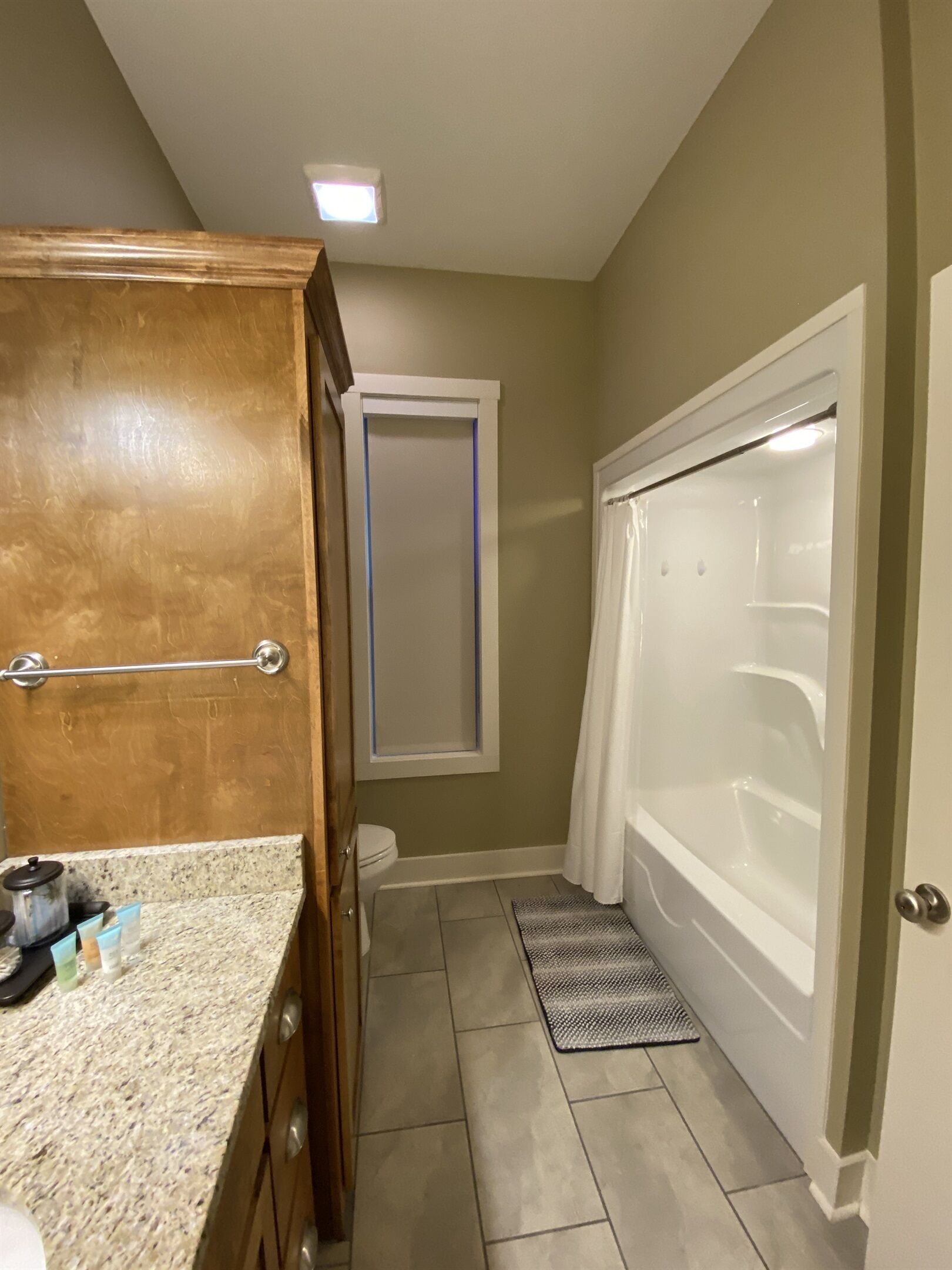 Une salle de bain avec un meuble-lavabo en bois, une douche avec un rideau et un petit tapis sur le sol.