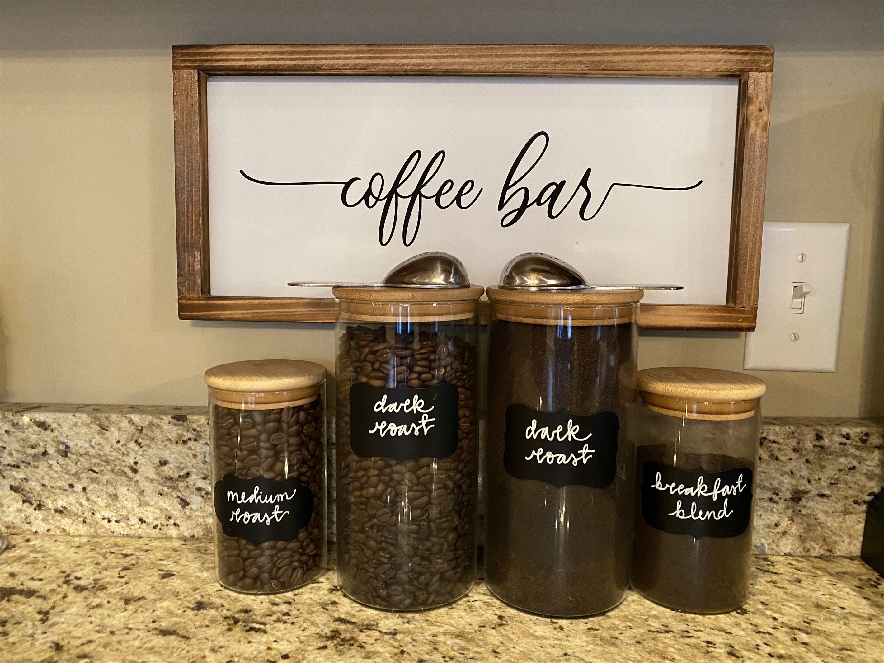 A coffee bar sign with four labeled jars of coffee beans on a countertop.