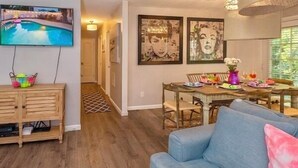 A living room with a blue sofa, wooden cabinet, and a TV mounted on the wall. - 5mins Steps to Beach | Fenced Heated Pool w/ Grill (Miramar Beach)