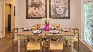 A dining area with a wooden table set for four, surrounded by chairs. There are two framed artworks on the wall above the table. - 5mins Steps to Beach | Fenced Heated Pool w/ Grill (Miramar Beach)