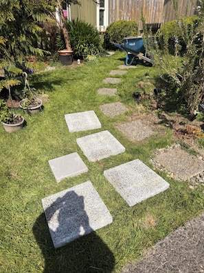 A garden with stepping stones, potted plants, and a wheelbarrow.