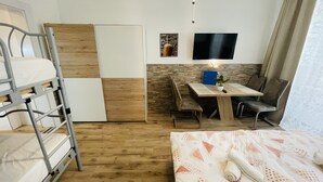 Una stanza funzionale con letti a castello, una scrivania, una sedia, una TV e un piccolo tavolo con una pianta.