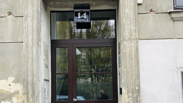 Un edificio con un'ampia finestra ad arco sopra una porta marrone scuro, una insegna con su scritto "14 Kempelen G." e una piccola finestra a destra.