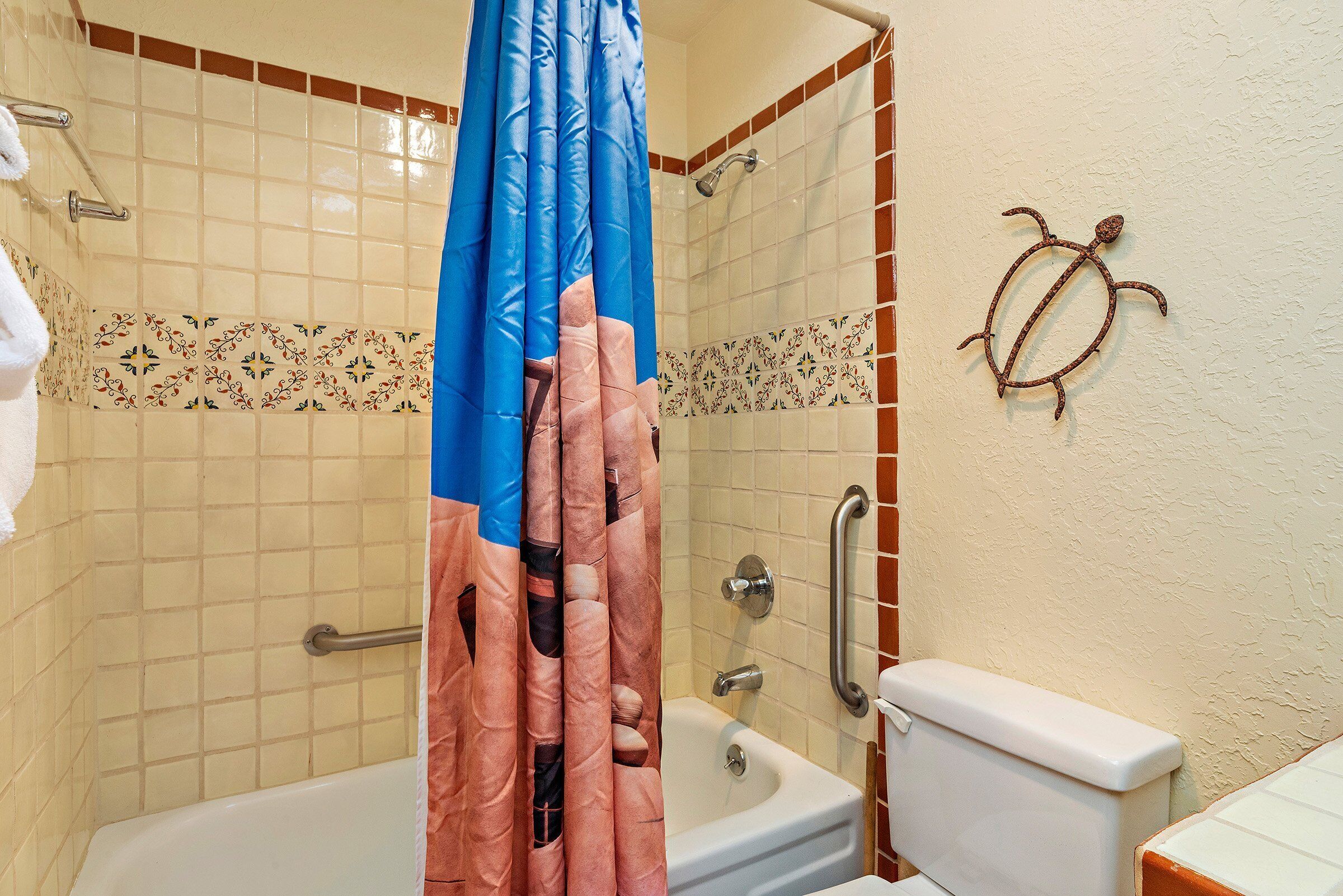 Ein Badezimmer mit Badewanne, Dusche und Toilette. Die Wände sind mit dekorativen Fliesen versehen und es gibt einen Handtuchhalter.