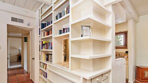 Ein geräumiger Raum mit einem großen, weißen Bücherregal voller Bücher, einer Holzschrank und einem Fliesenboden.