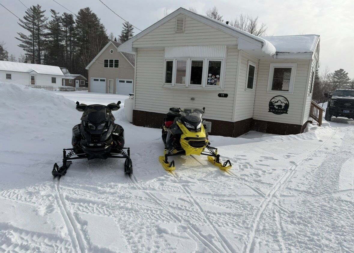 Deux motoneiges sont garées devant une maison qui a un garage.