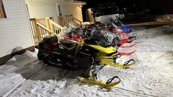 Snowmobiles are parked outside this house, which features a deck and a window.