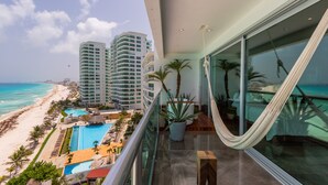 A balcony with a view of a beach and a pool, a hammock, and a potted plant. - The Quarry Cancun- luxury oceanfront studio (Cancún)