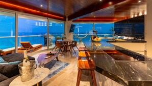 A modern kitchen with a marble countertop, wooden stools, and a view of the ocean. - The Quarry Cancun- luxury oceanfront studio (Cancún)