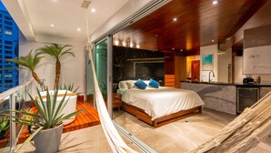 A modern bedroom with a large bed, a hammock, and a balcony with plants. - The Quarry Cancun- luxury oceanfront studio (Cancún)