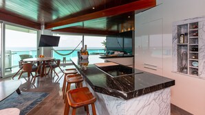 A modern kitchen with a marble countertop, wooden ceiling, and a view of the ocean. - The Quarry Cancun- luxury oceanfront studio (Cancún)