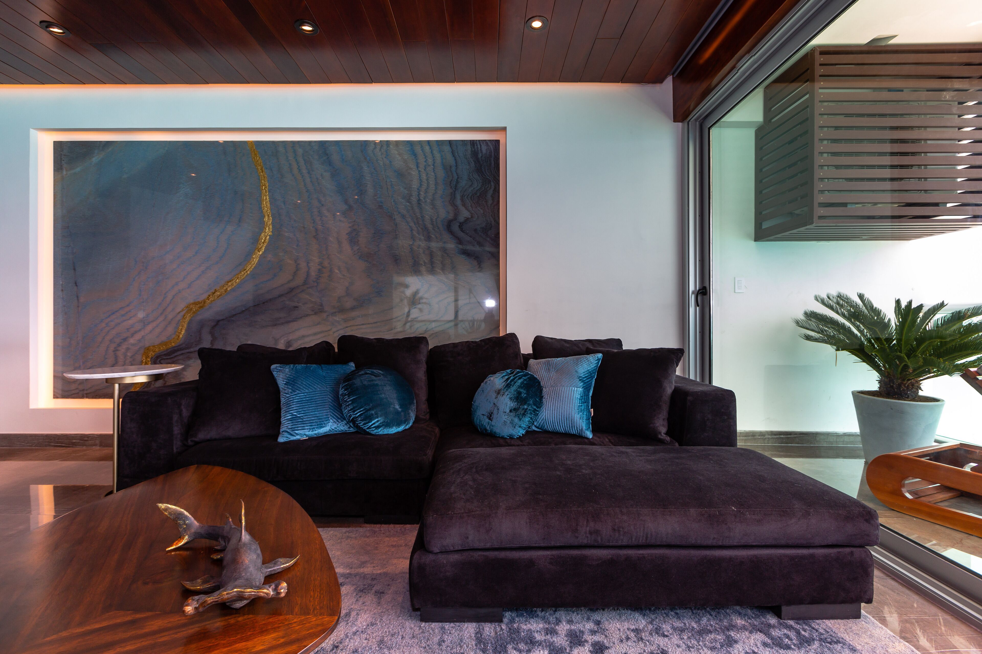 Una sala de estar moderna con un sofá modular de color oscuro, una mesa redonda de centro y un cuadro abstracto grande en la pared.