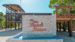 En skylt för ”The Big Beach House”, med en fasad av sten och en träkonstruktion i bakgrunden.
