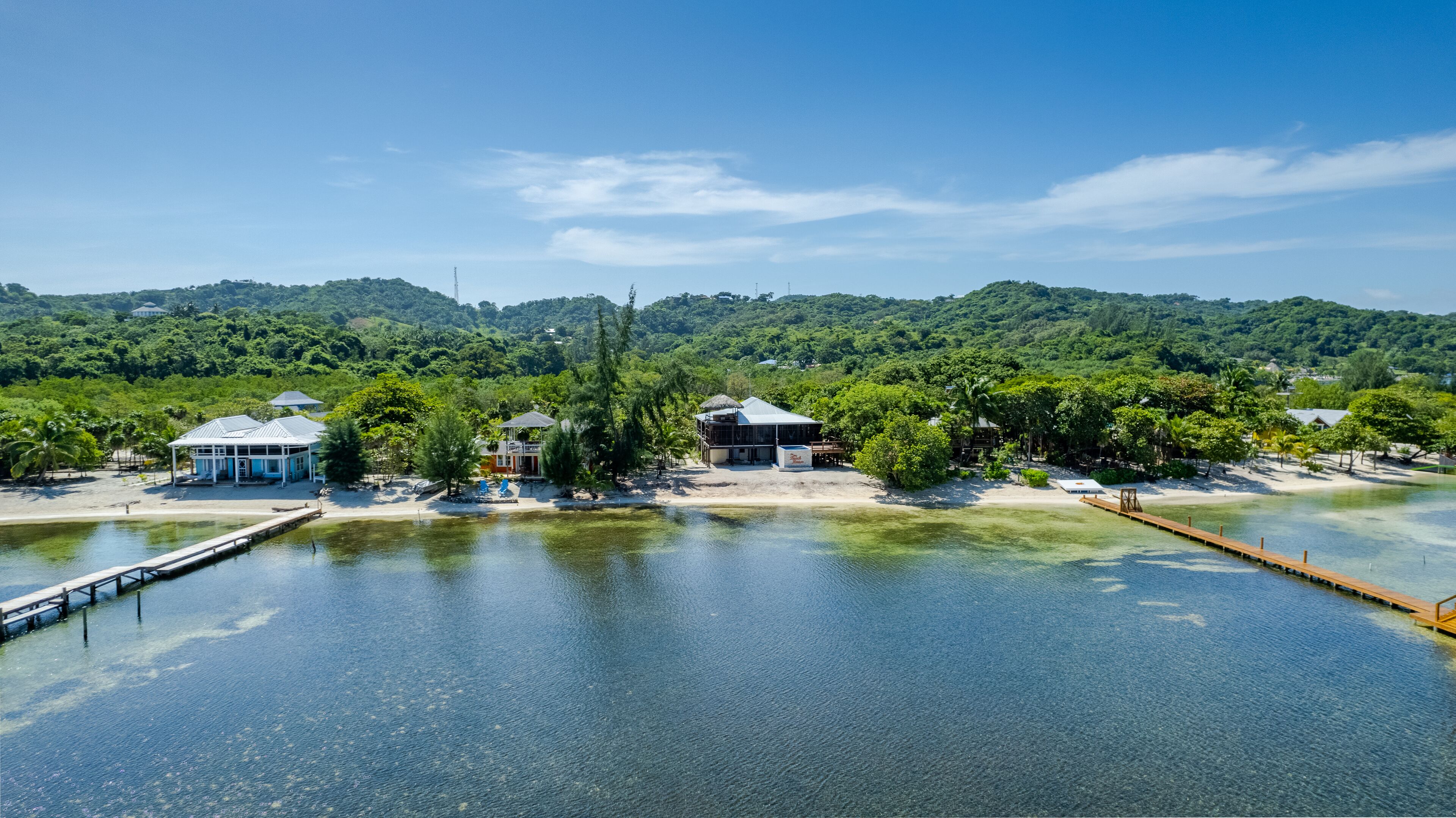 A coastal property with a dock, beach, and structures surrounded by lush greenery.