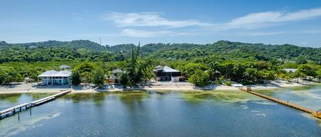 A coastal property with a dock, beach, and structures surrounded by lush greenery.