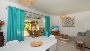 Una sala de estar moderna con comedor, sofá, televisor y vistas al exterior.