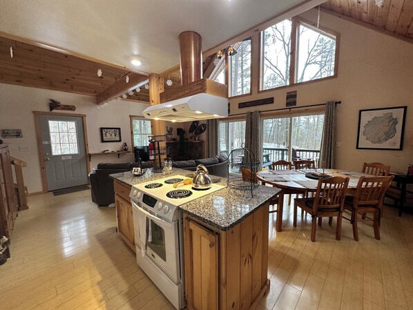 A spacious kitchen with a central island, wooden cabinets, and a large window overlooking a deck.