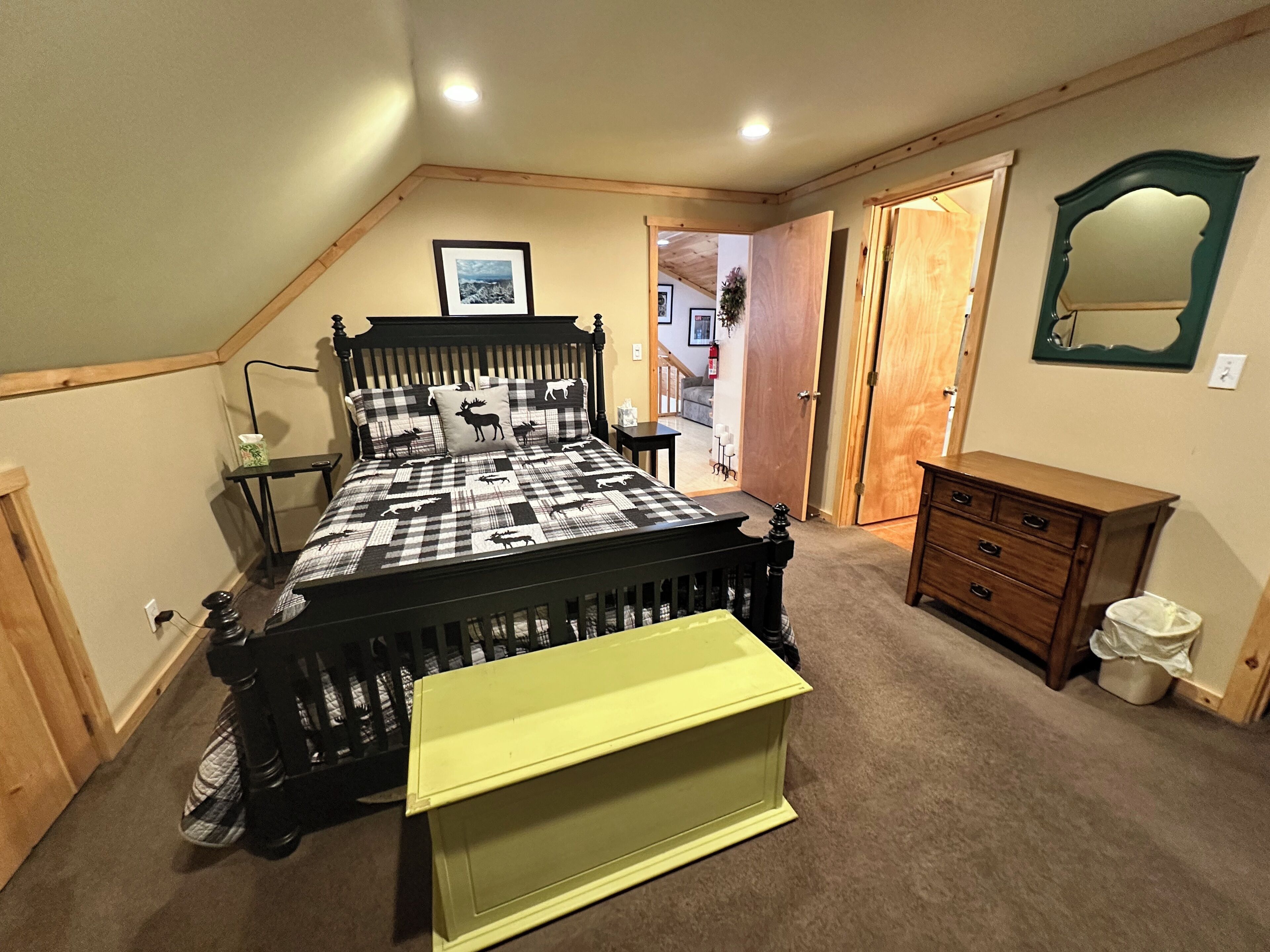 Een slaapkamer met een bed, een dressoir, een spiegel en een deur naar een andere kamer.