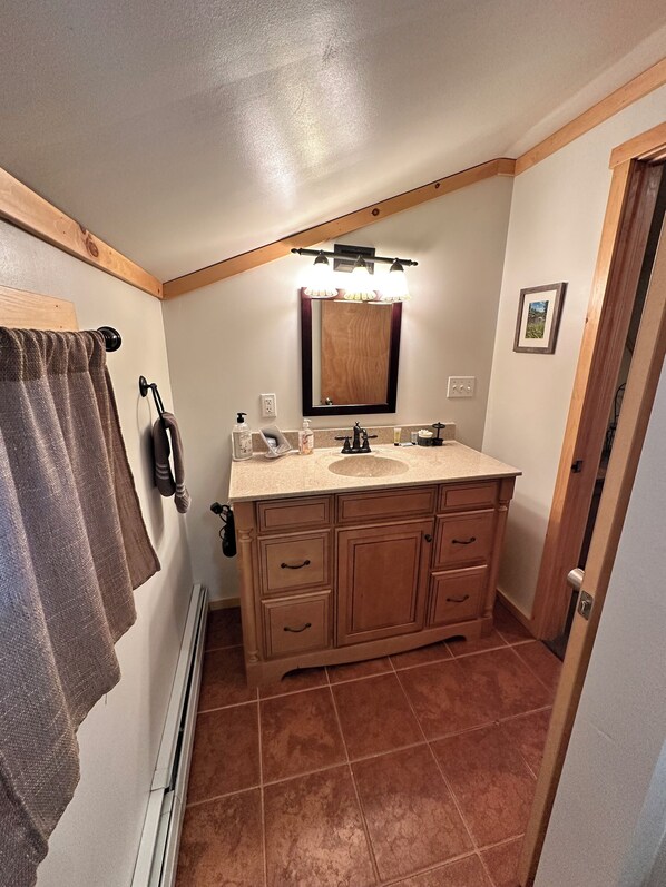 A bathroom with a wooden vanity, a mirror with lights, a towel rack, and a door leading to another room.