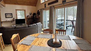 L’intérieur chaleureux d’un chalet avec une table à manger en bois, disposée pour quatre personnes, un ventilateur de plafond et de grandes fenêtres offrant une vue sur l’extérieur.