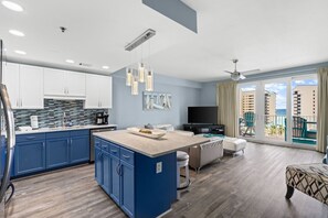 A modern hotel room with a kitchen, a dining area, a living room, and a balcony with a view of the ocean.
