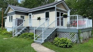 Uma casa móvel de dois andares com varanda da frente, escada e área de deck cercada.
