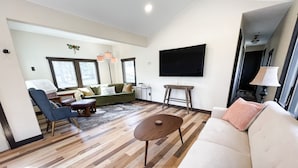 Uma sala de estar moderna com sofá, poltrona, mesa de centro e televisão na parede.