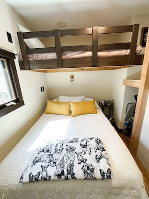 A bunk bed with a wooden headboard, a window, and a bedside table with a lamp.