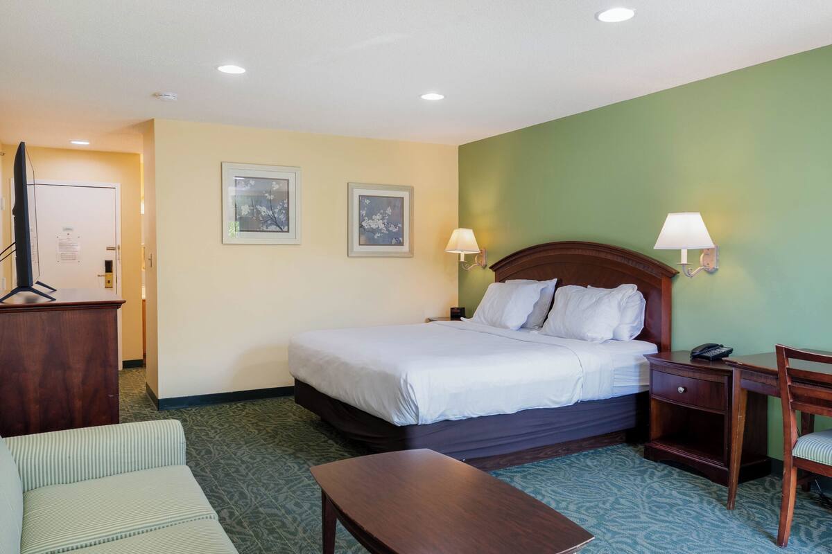A hotel room with a bed, bedside lamps, a desk, a chair, a TV, and framed pictures on the wall.