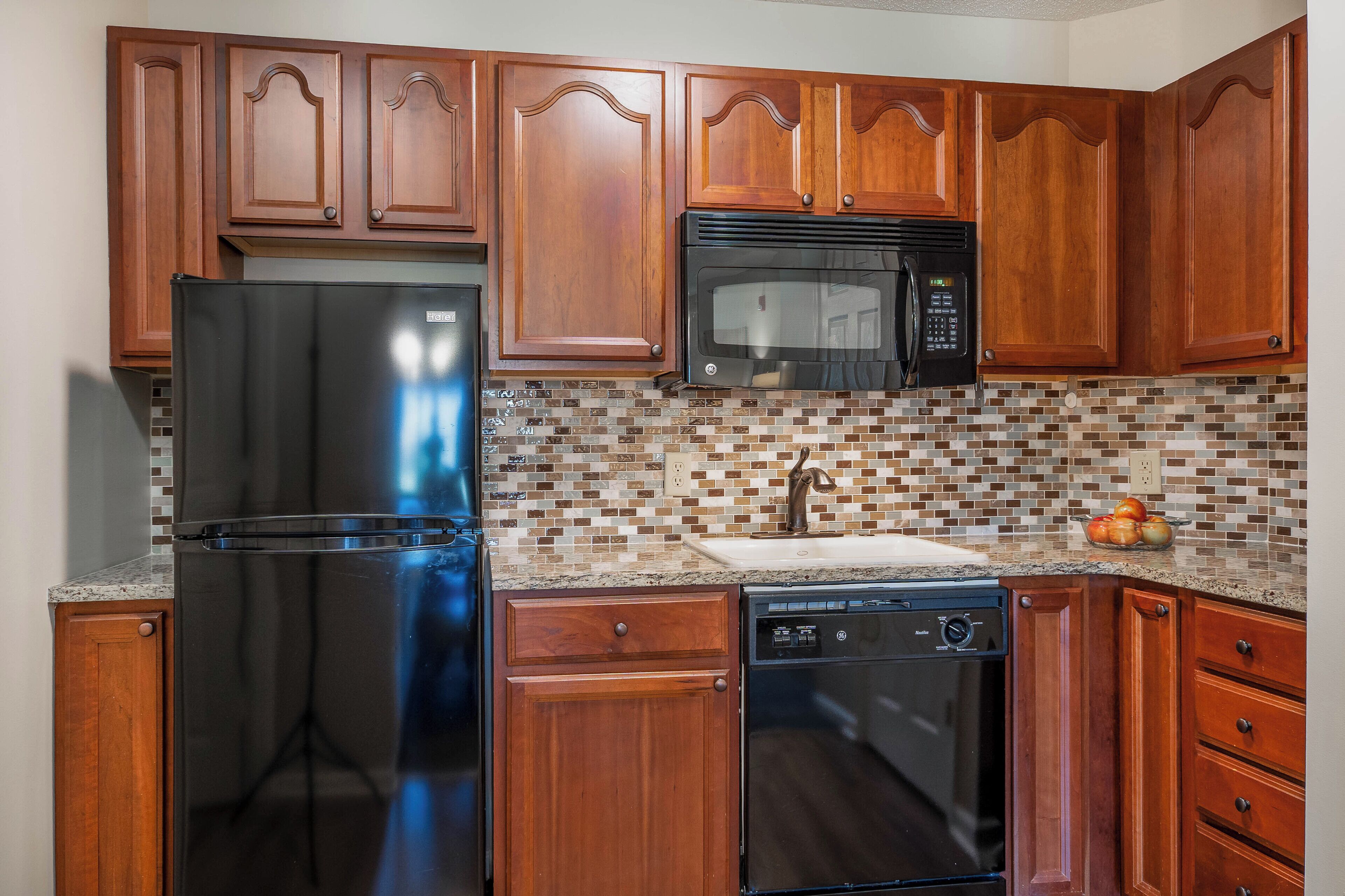 A kitchen with wooden cabinets, a stainless steel refrigerator, a microwave, and a dishwasher.