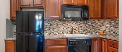 A kitchen with wooden cabinets, a stainless steel refrigerator, a microwave, and a dishwasher.