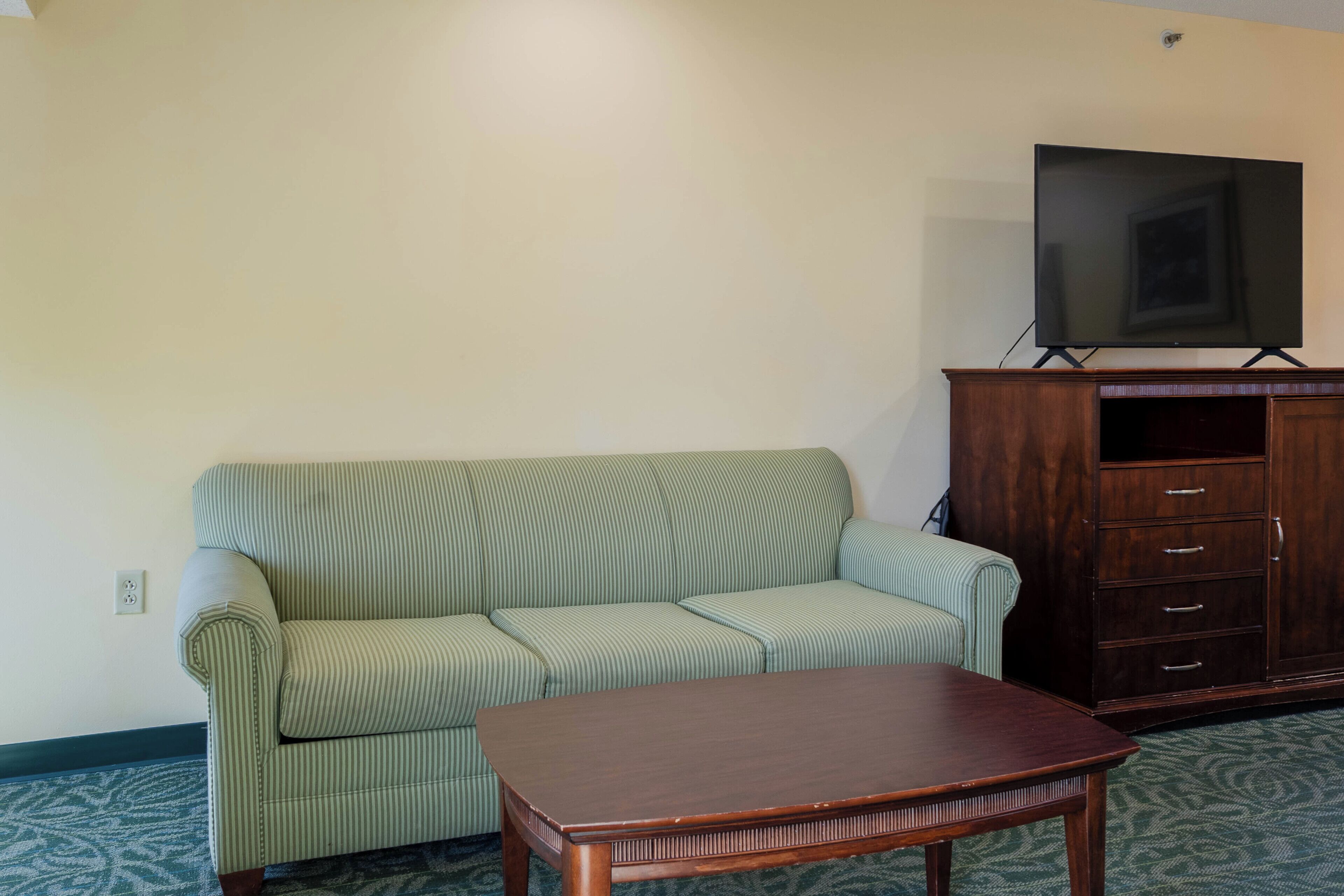 A room with a green-striped sofa, a wooden coffee table, a TV on a stand, and a wooden cabinet.