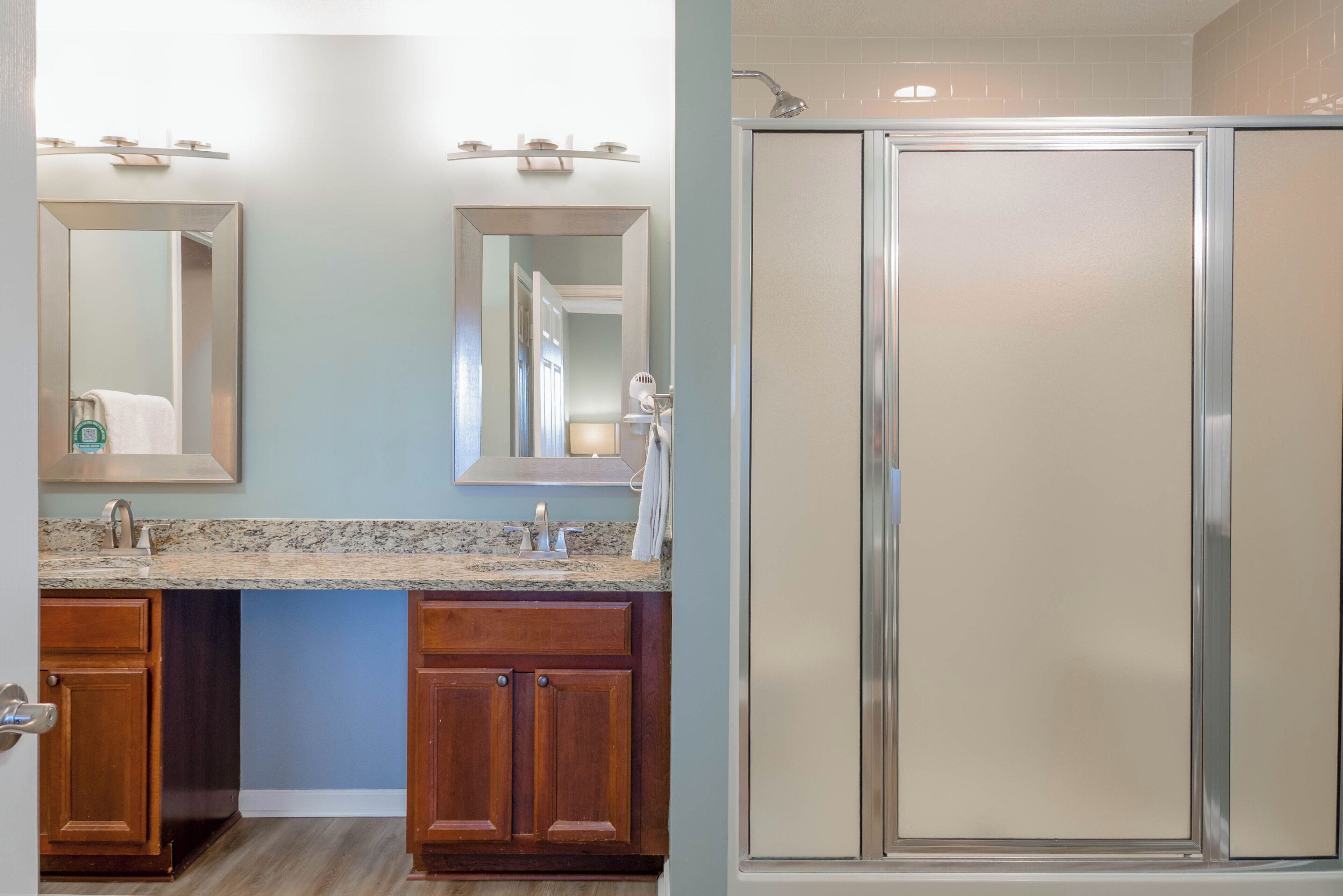 A bathroom with a shower, a sink with a mirror, and wooden cabinets.