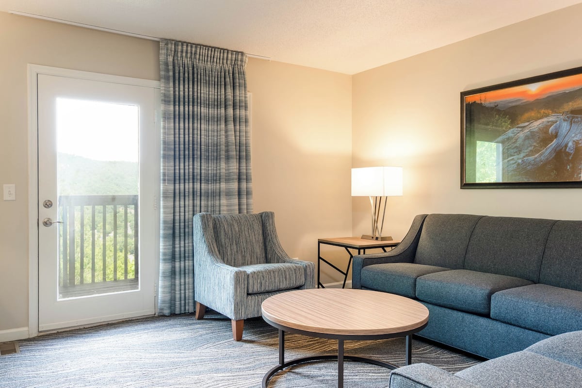 A hotel room with a sofa, armchair, small table, and a painting on the wall.