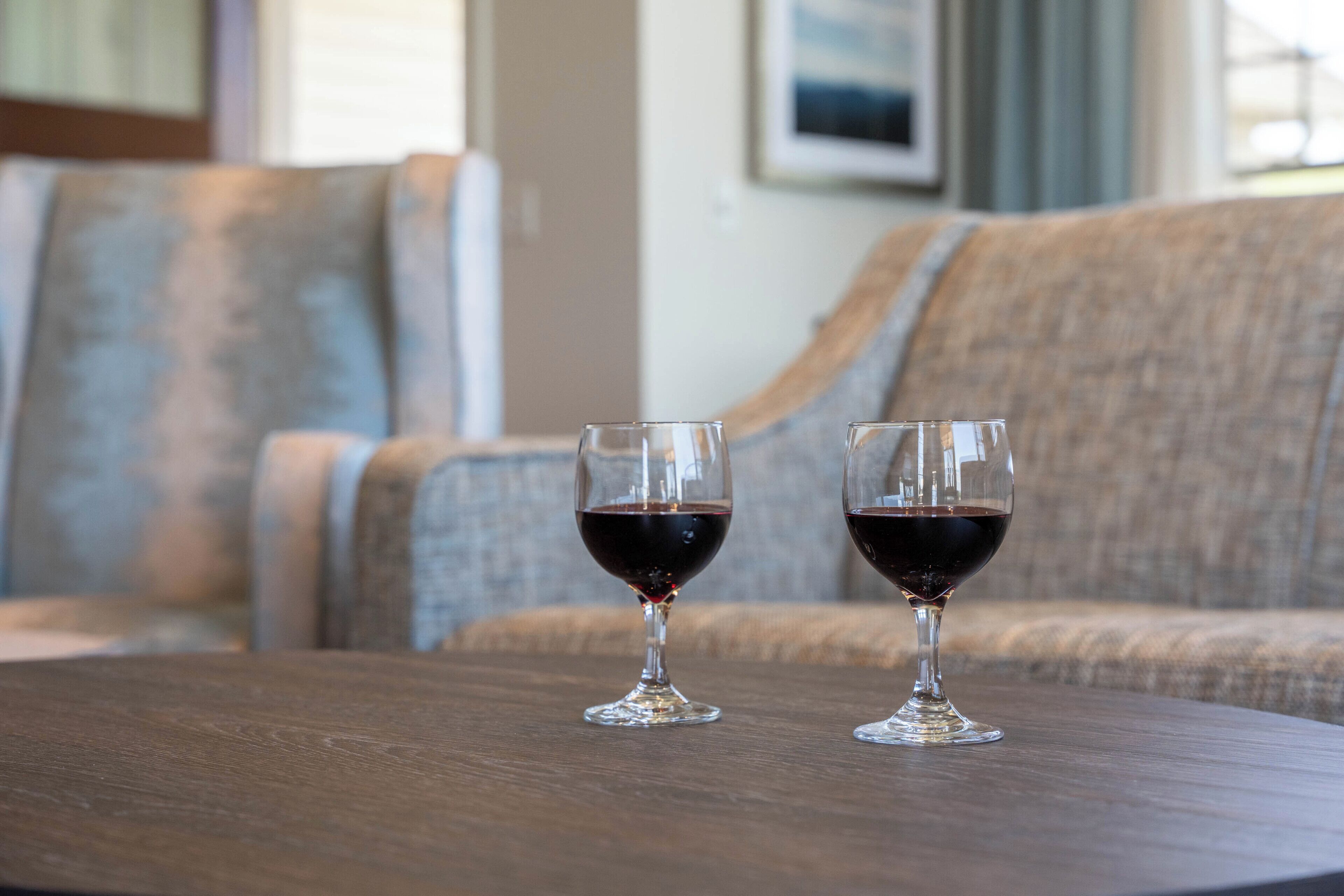 Two wine glasses on a wooden table with a sofa in the background.