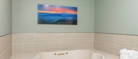 A bathroom with a large bathtub, a sink, and a wall-mounted painting of a landscape.