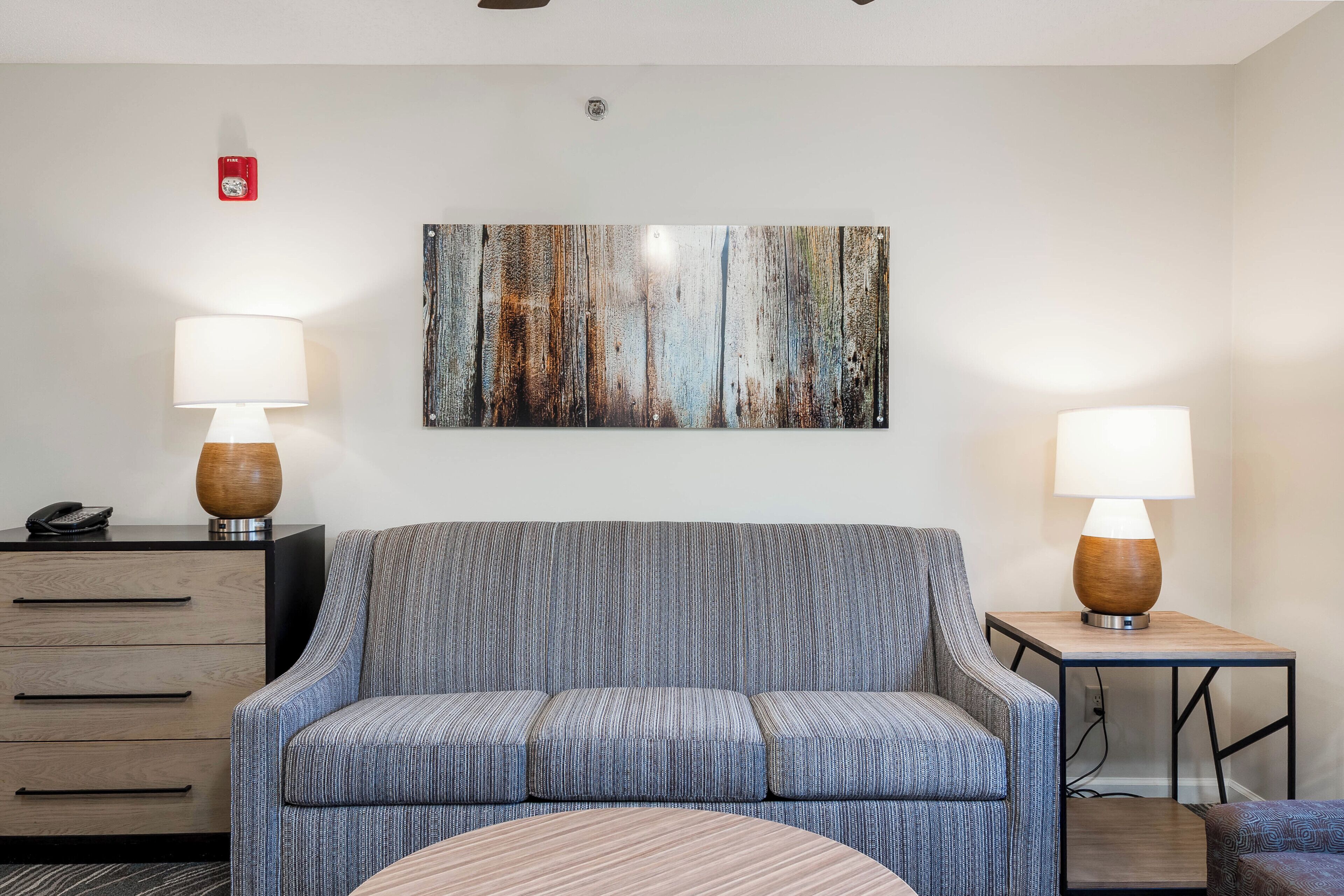 A room with a sofa, two side tables with lamps, a wall-mounted artwork, and a desk with a telephone.