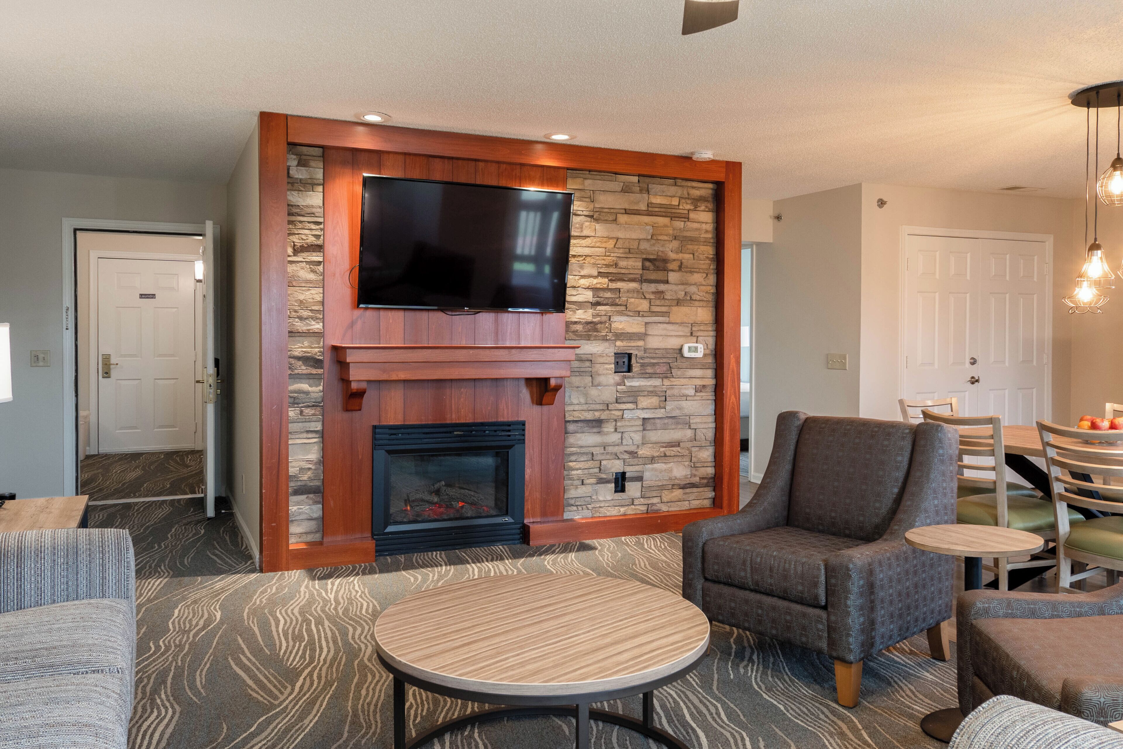 A living room with a stone fireplace, a flat-screen TV, a round coffee table, and a comfortable armchair.