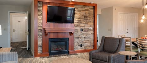 A living room with a stone fireplace, a flat-screen TV, a round coffee table, and a comfortable armchair.