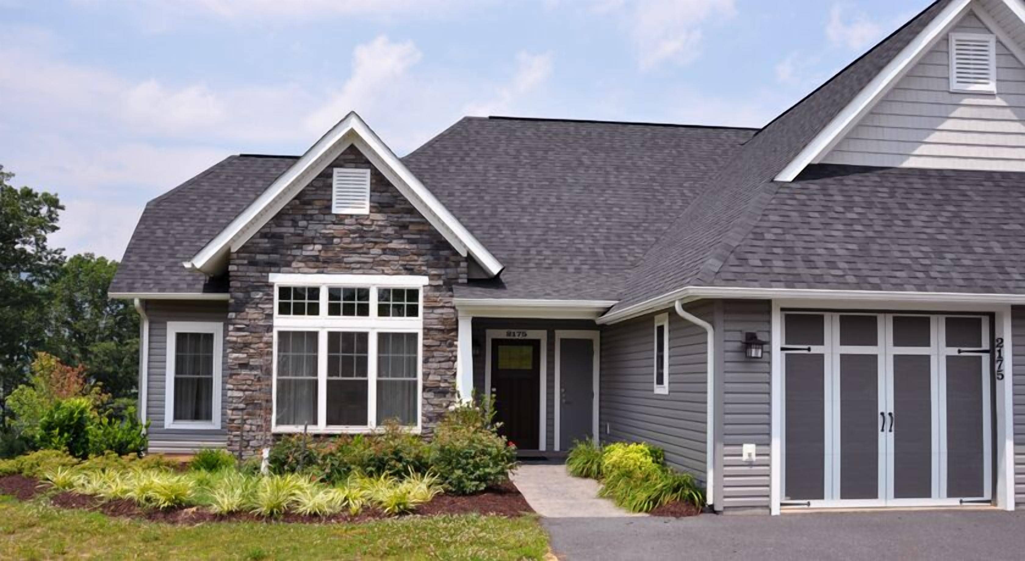 A modern two-story house with a stone facade, a large front window, and a garage.