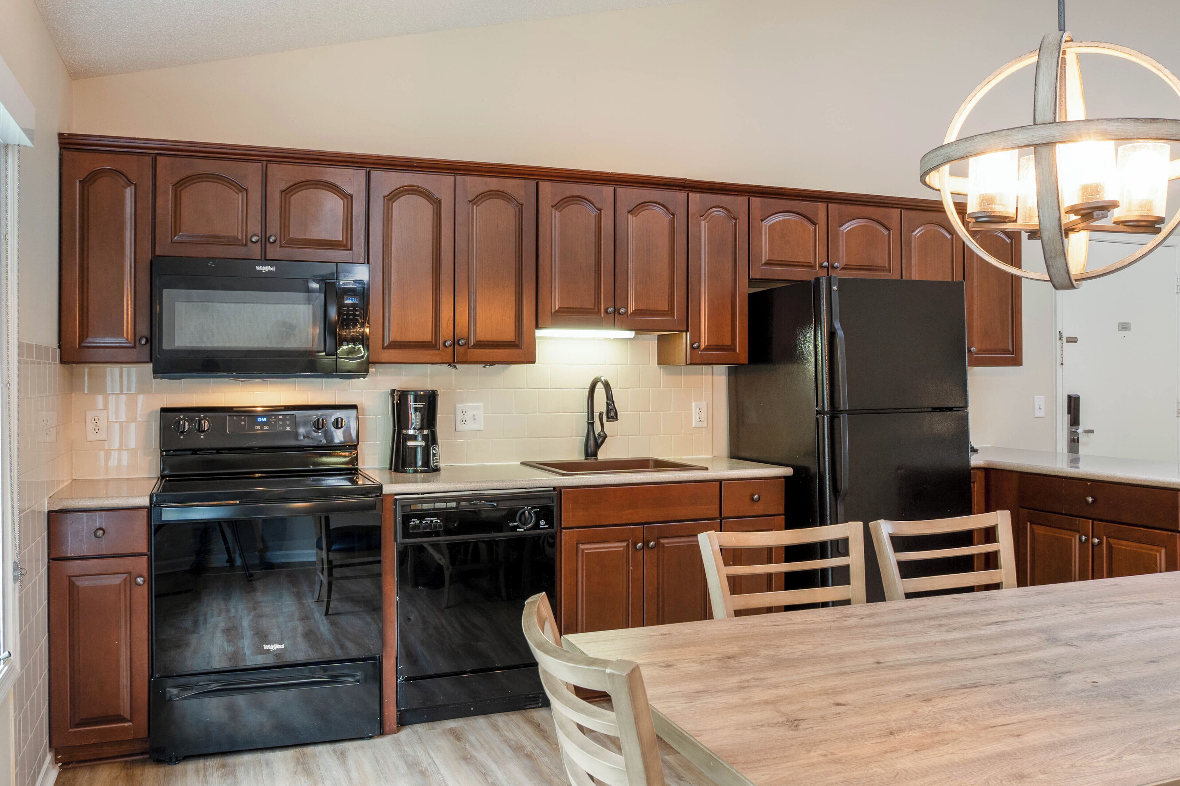 Une cuisine avec des meubles de rangement en bois, un micro-ondes noir, une cuisinière, un lave-vaisselle, un évier et une table à manger avec des chaises.