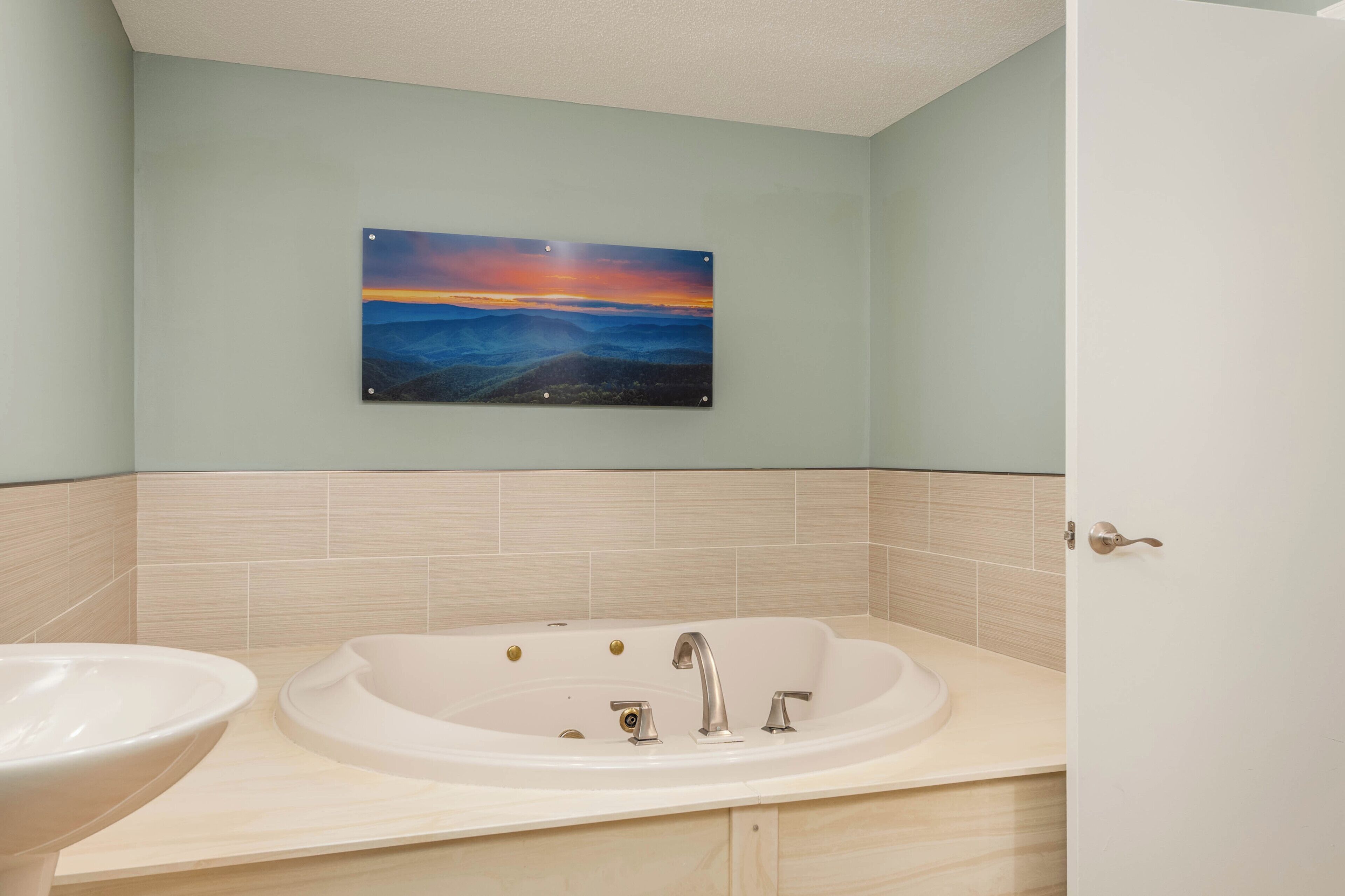 A bathroom with a large bathtub, a sink, and a wall-mounted painting.