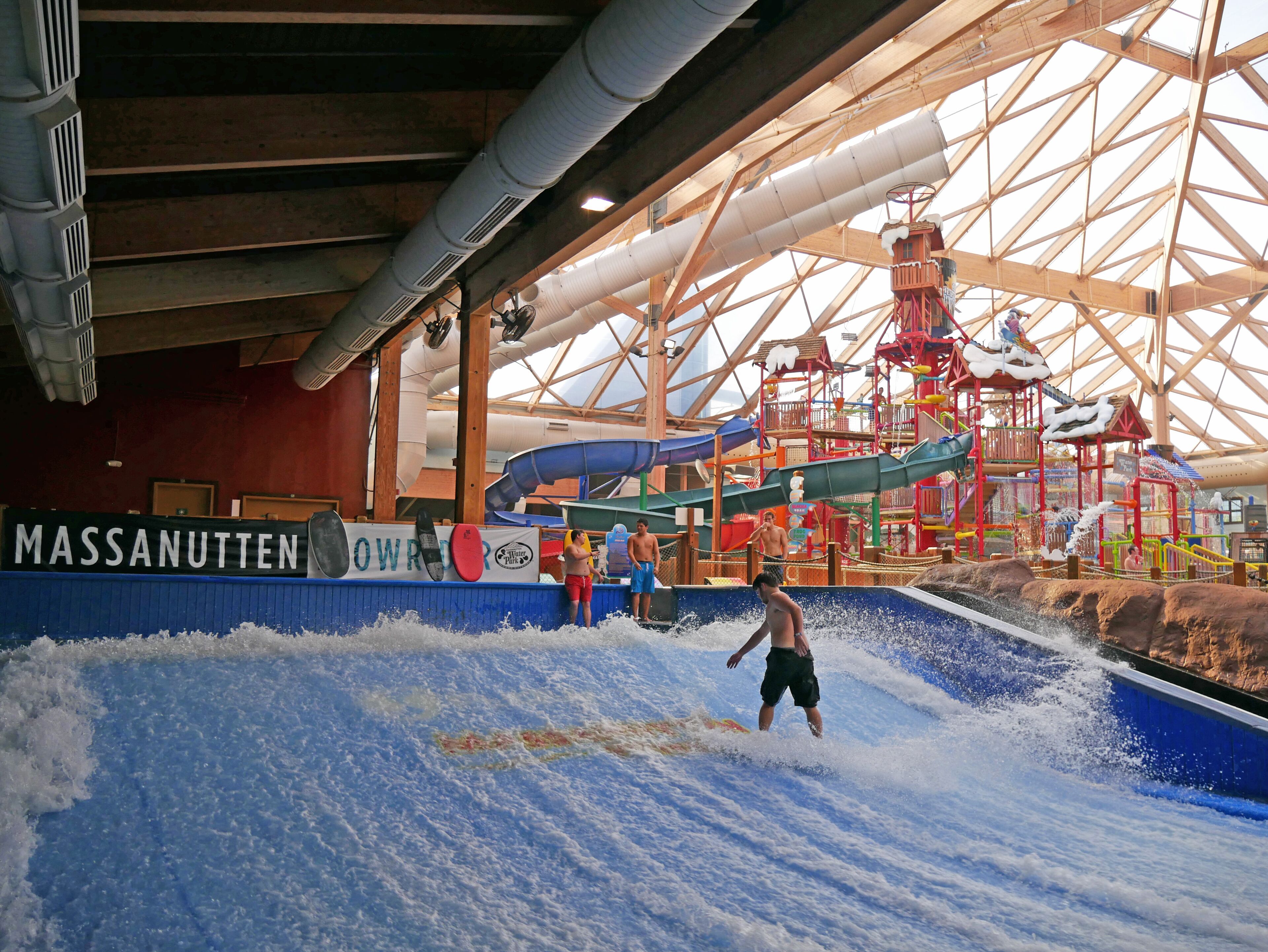An indoor water park with a wave pool, slides, and a wooden play structure.