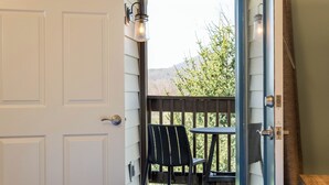 A room with a bed, a window with a view of greenery and mountains, a chair, and a table. - Massanutten Resort (McGaheysville)