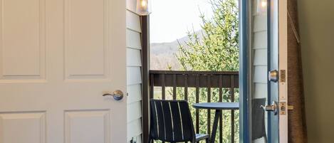 A room with a bed, a window with a view of greenery and mountains, a chair, and a table.