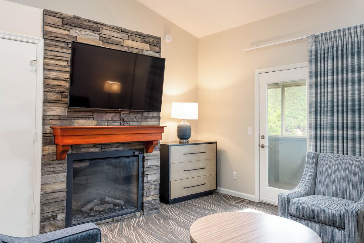 A living room with a stone fireplace, a flat-screen TV, a lamp, a chair, and a sliding glass door.