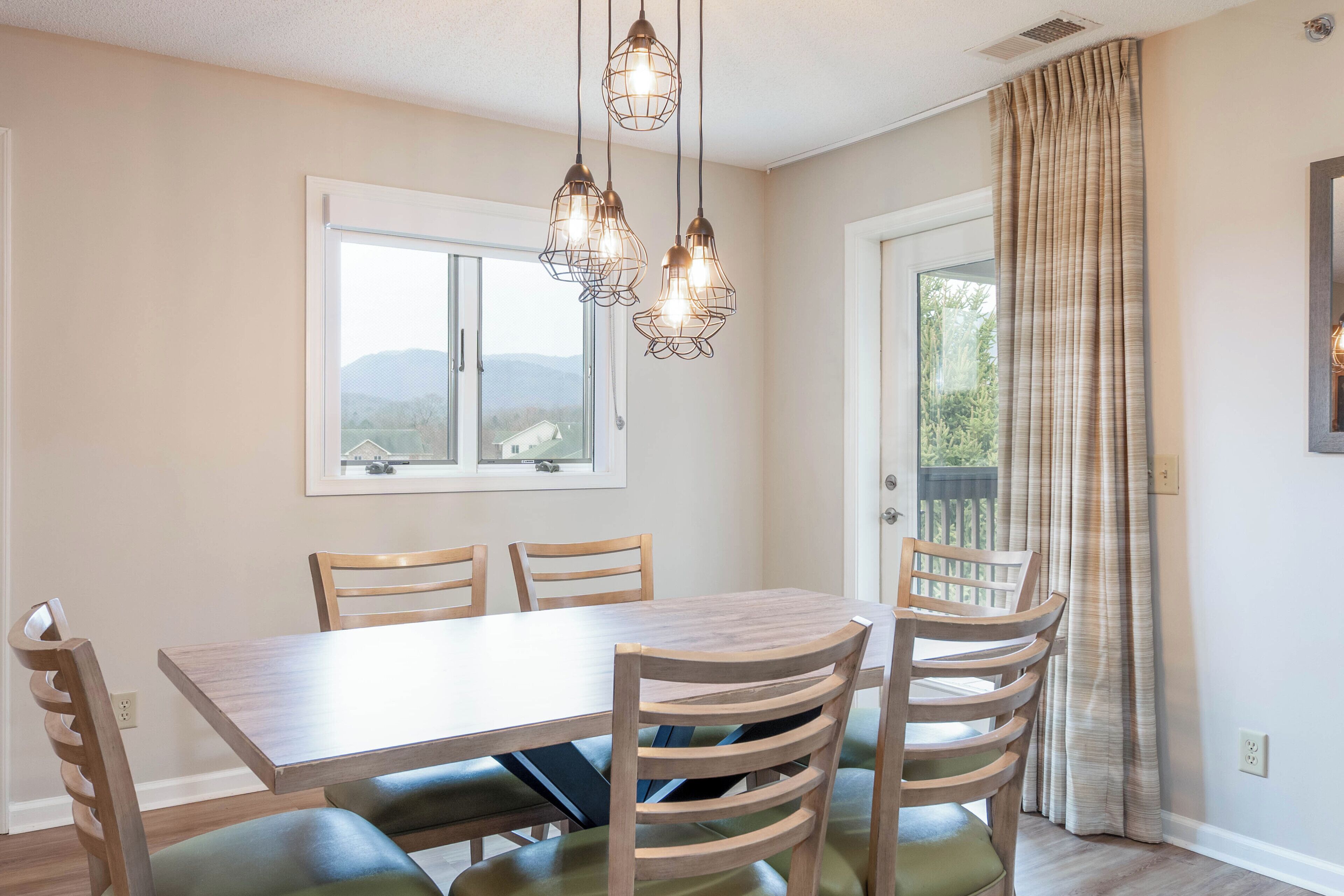 A dining area with a wooden table, four chairs, and a view through a window.