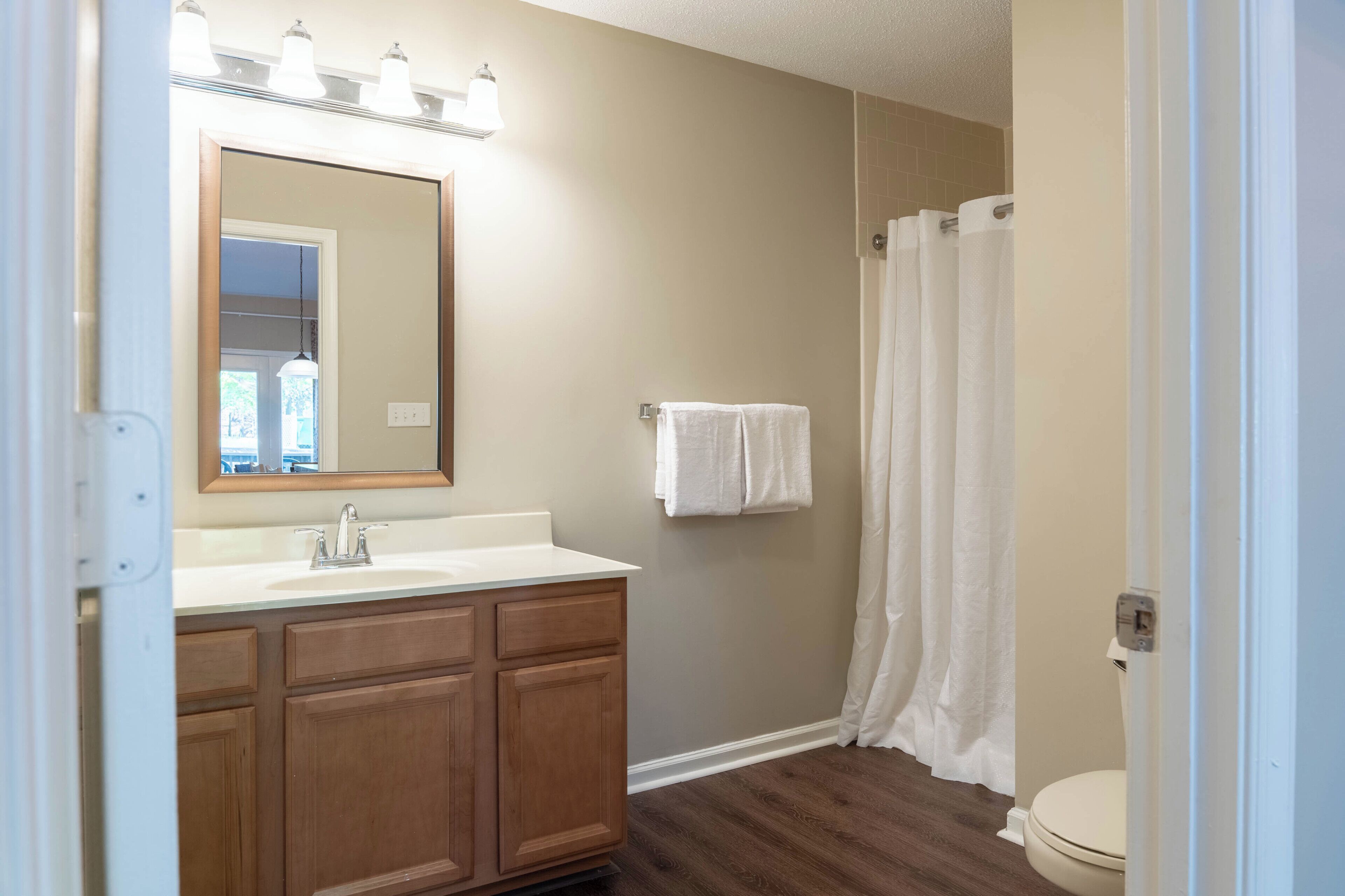 A bathroom with a wooden vanity, a mirror, a sink, a toilet, and a shower curtain.